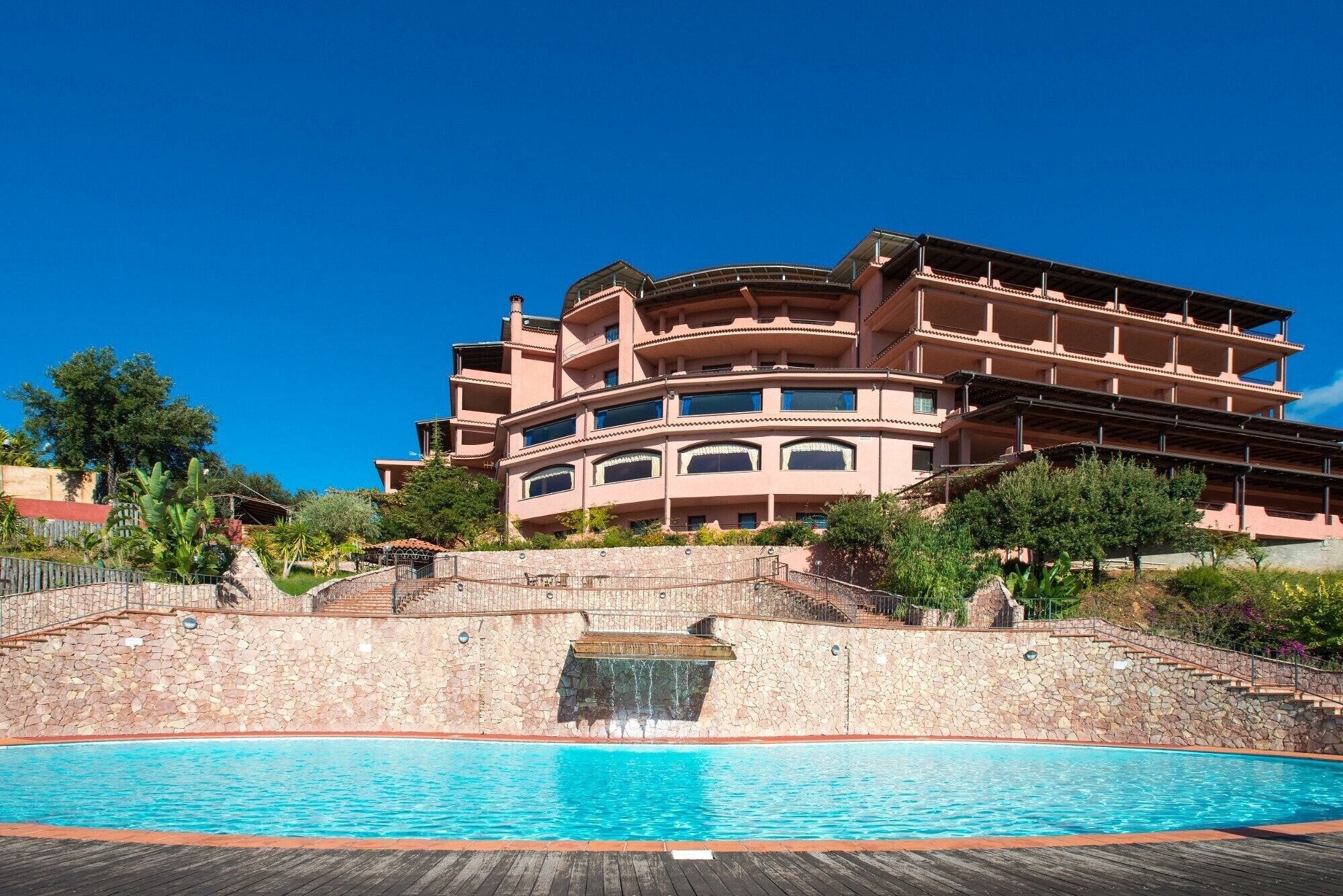 Un hotel a più piani con piscina, pareti in pietra e un cielo azzurro limpido.
