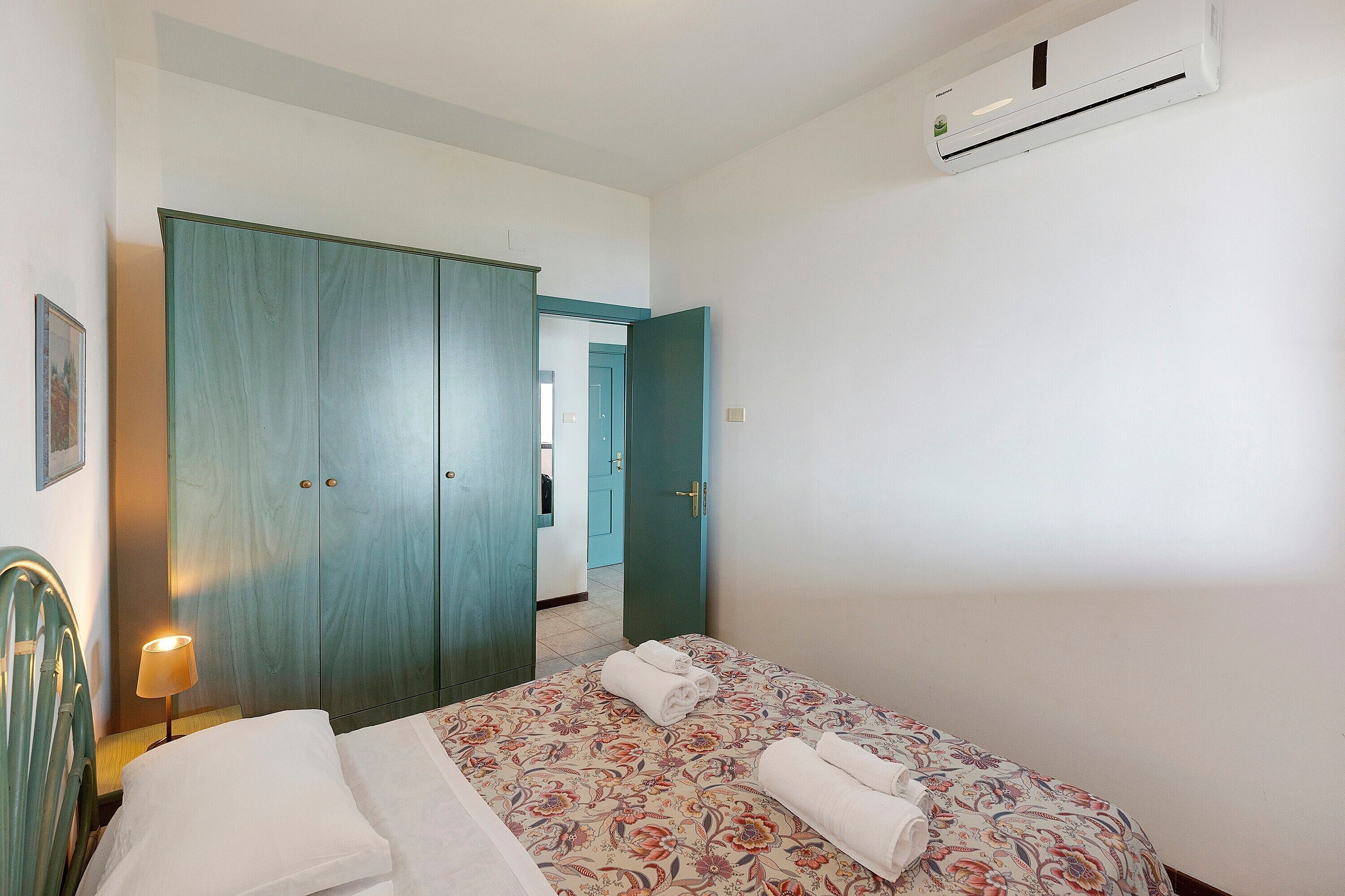 A hotel room with a bed, a wardrobe, a door, and an air conditioning unit.