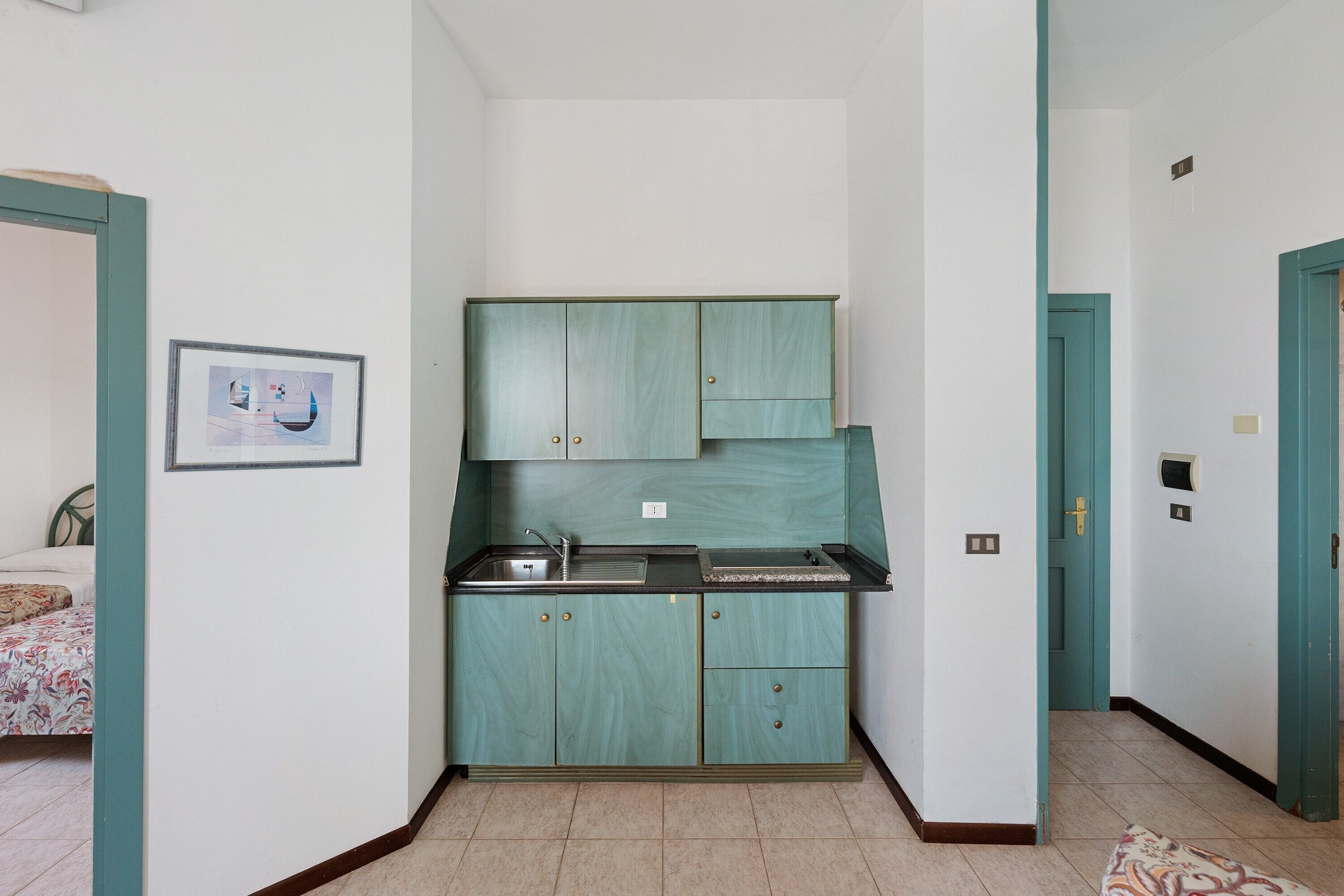 Cocina compacta con armarios color turquesa, un lavamanos y un cuadro en la pared.