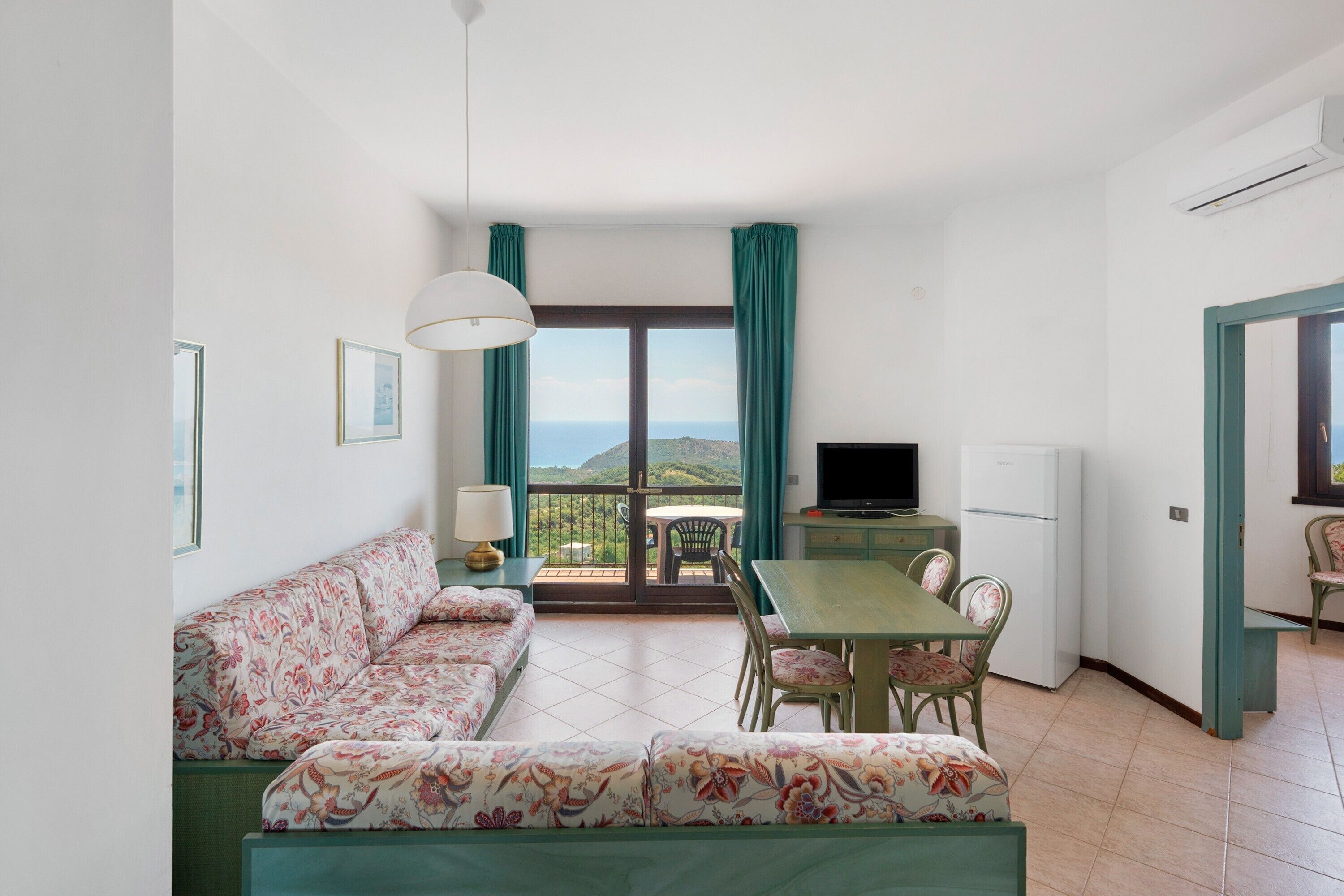 A room with a sofa, dining table, chairs, a TV, and a refrigerator.