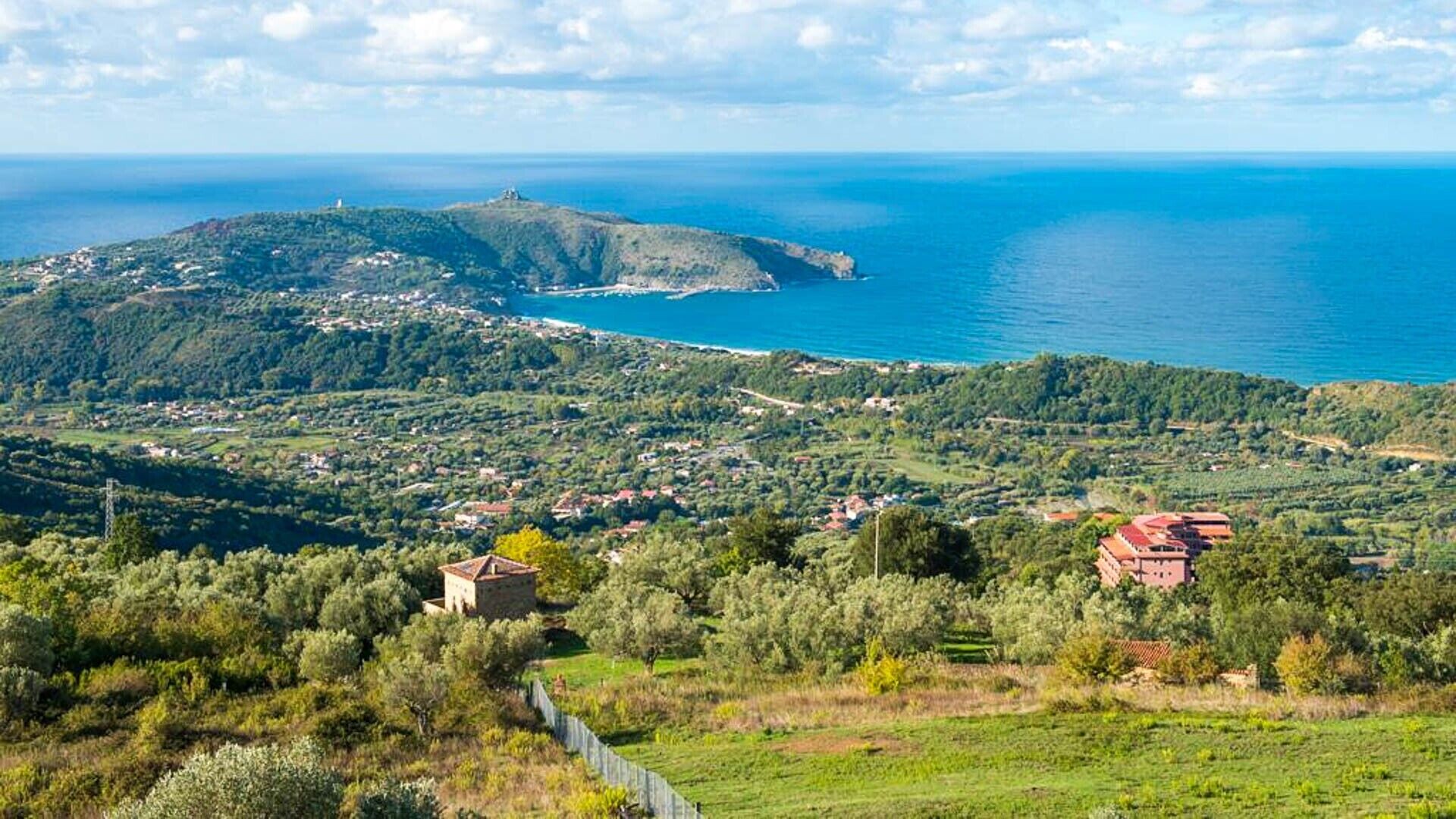 A coastal landscape with a hill, a small village, and a clear view of the sea.