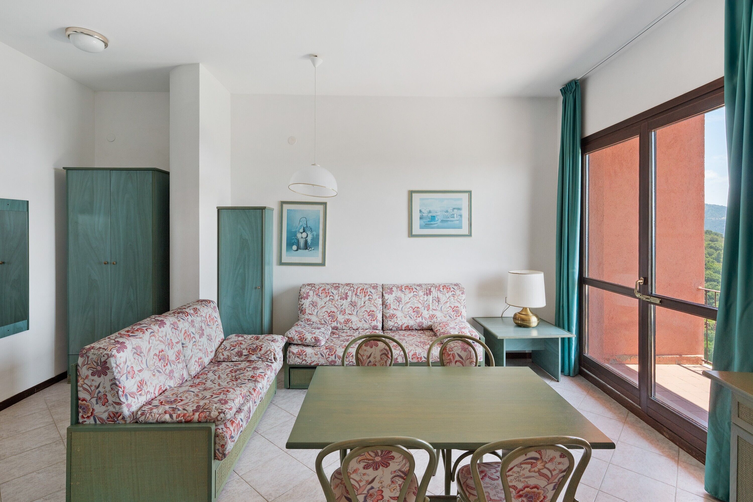 A room with a sofa set, a dining table, chairs, a lamp, and artwork on the walls.