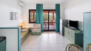 Una habitación con sofá, televisión, armario y puerta corrediza de vidrio que da a un espacio exterior.