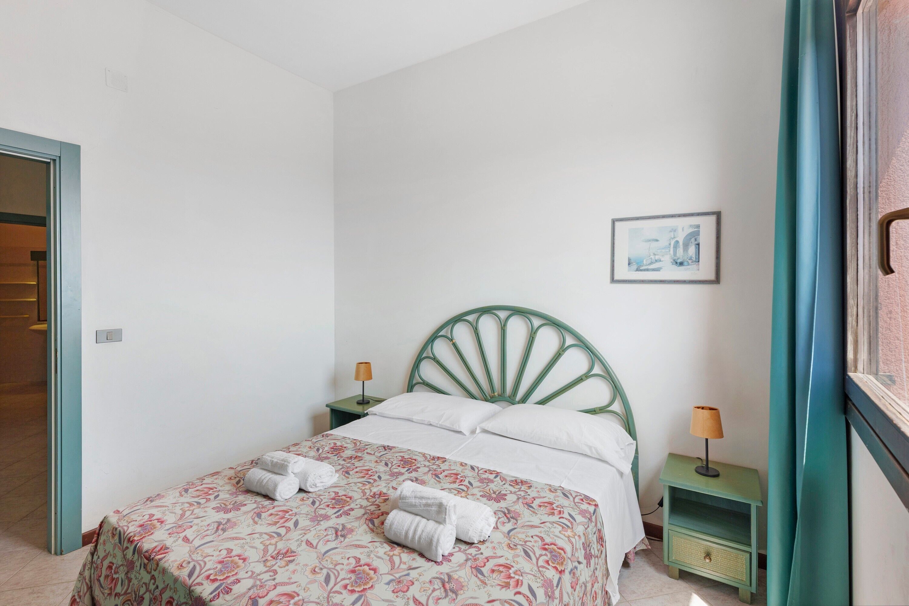 Een slaapkamer met een bed, twee nachtkastjes, een aan de muur hangend schilderij en een deur.