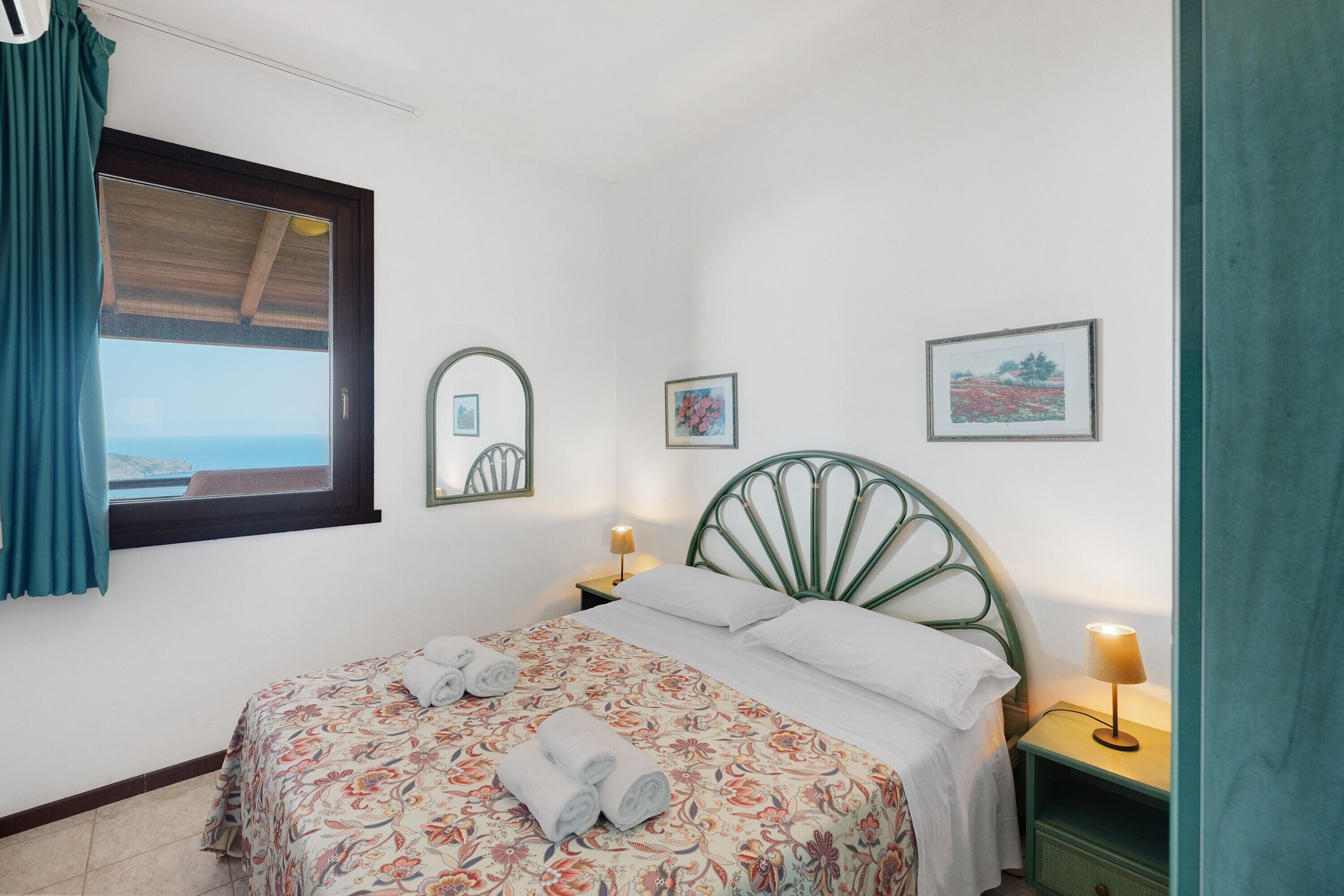 Une chambre à coucher avec un lit, deux tables de chevet, une fenêtre avec des rideaux et trois tableaux encadrés accrochés au mur.