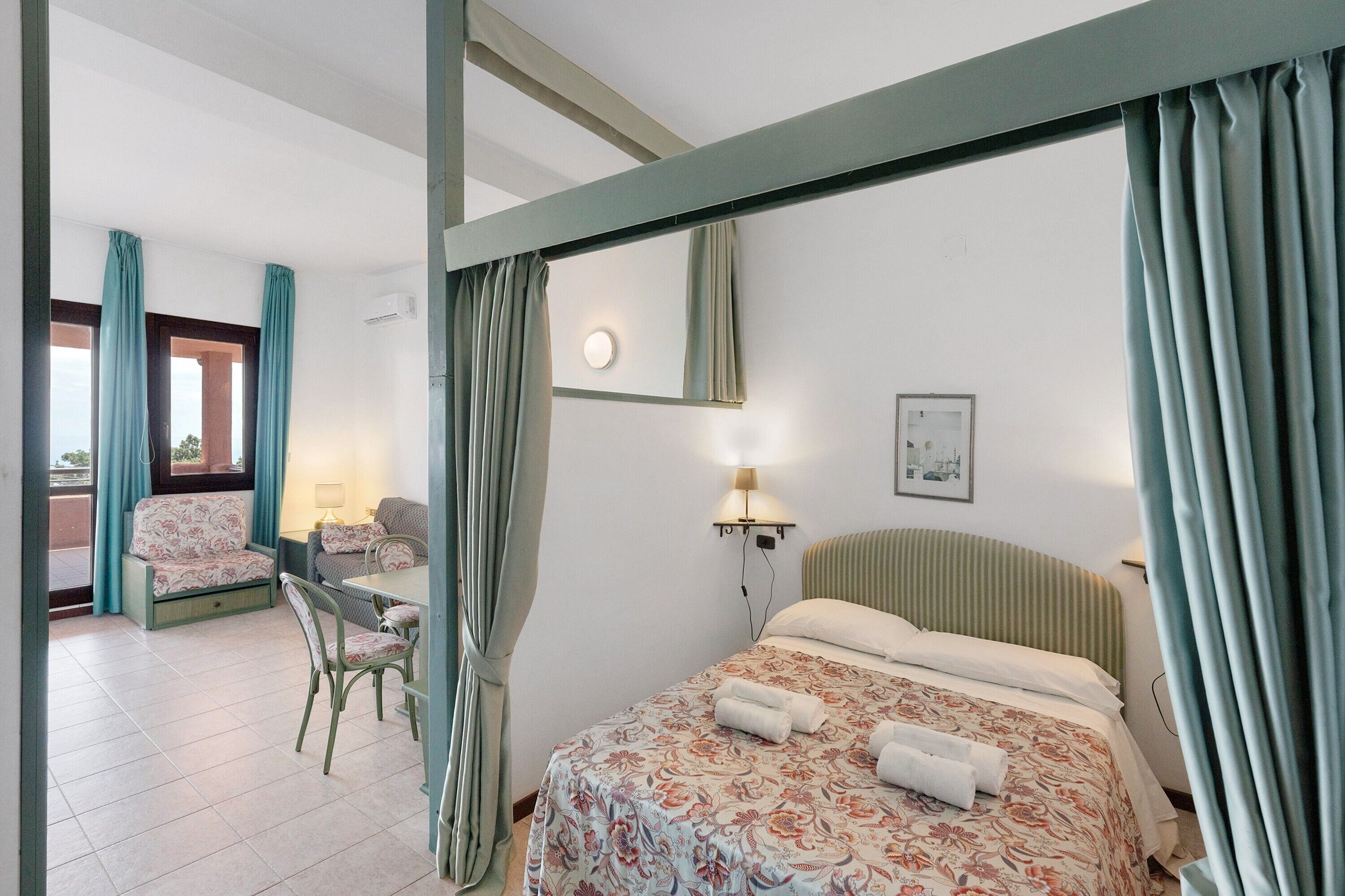 A hotel room with a bed, a chair, a desk, and a window with curtains.