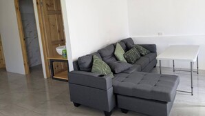 Ein modernes Wohnzimmer mit einem grauen Ecksofa, einem kleinen weißen Tisch und einem Holzschrank mit einer Schale.