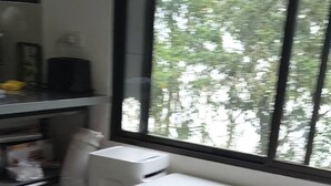 Ein Zimmer mit Schreibtisch und Stuhl, ein Fenster mit Blick auf Bäume und ein Fliesenboden.