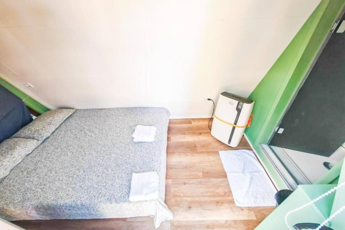Une petite pièce avec un lit, un mur vert, un plancher en bois et un bureau avec un ordinateur.