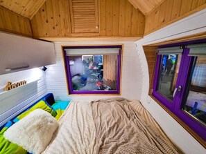 Een gezellige kamer met een bed, een raam met uitzicht op de straat, en een deur met een paarse omlijsting.