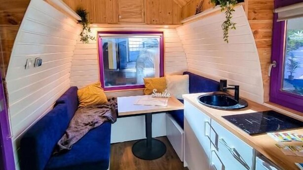 Un intérieur compact en bois, comprenant une kitchenette, un petit coin repas et une fenêtre offrant une vue.