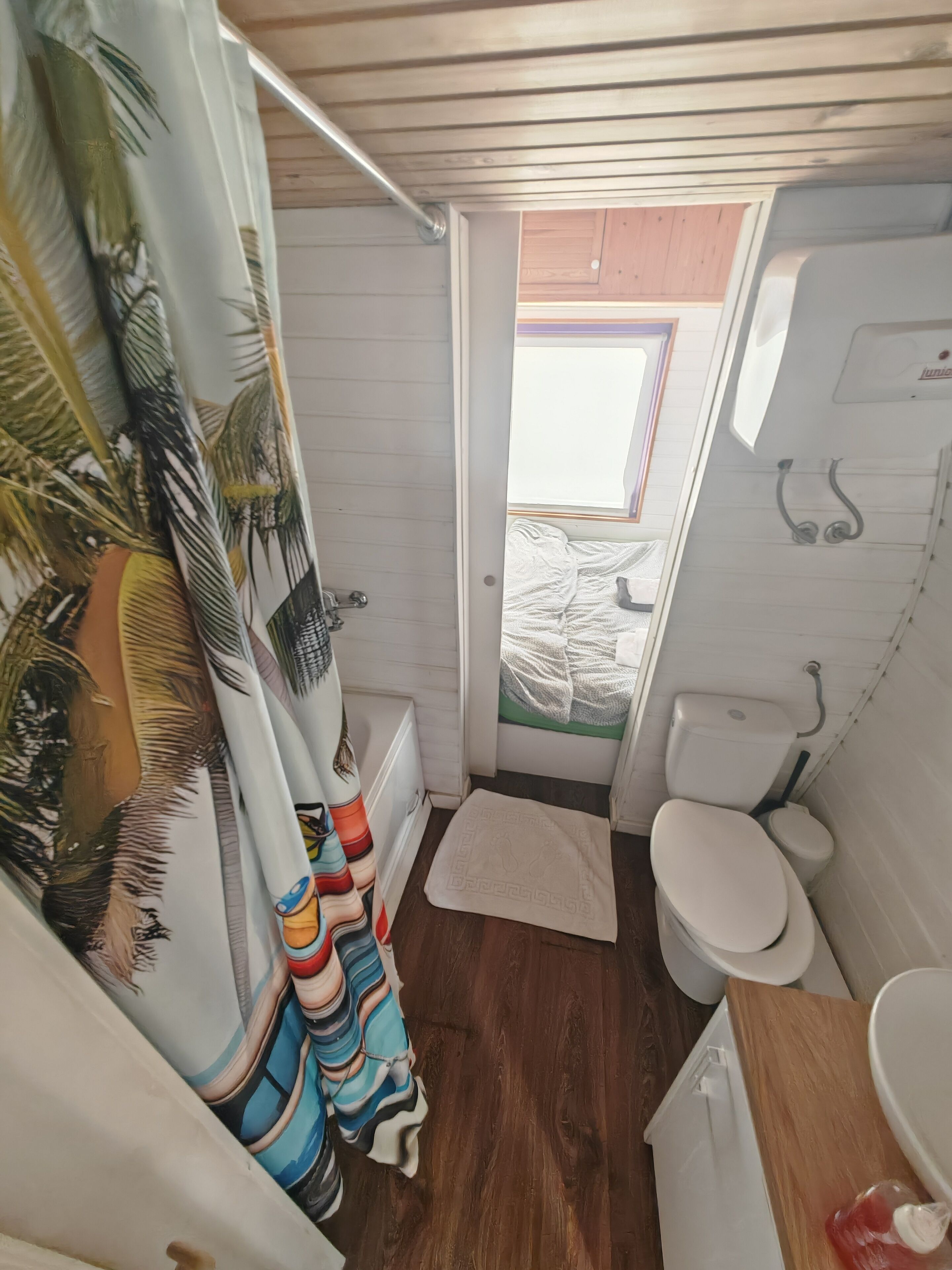 A compact bathroom with a wooden floor, a white toilet, a small sink, and a shower area.