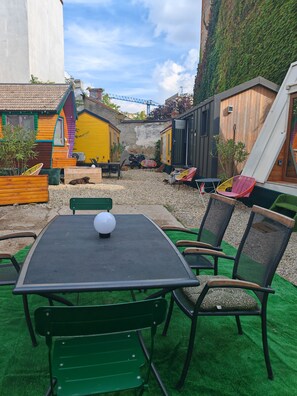 Een terras buiten met een tafel en stoelen, omgeven door kleurrijke gebouwen en een groene wand.