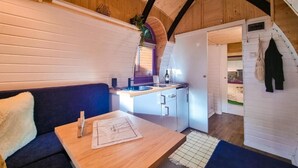 Une pièce chaleureuse avec un plafond en bois, un canapé bleu foncé, une table en bois et un petit coin cuisine équipé d’un évier et de placards.