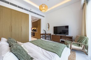 A modern hotel room with a large bed, a TV, a desk, and a dining area. - Bloomfields Supreme Stu In Azizi (Dubai)
