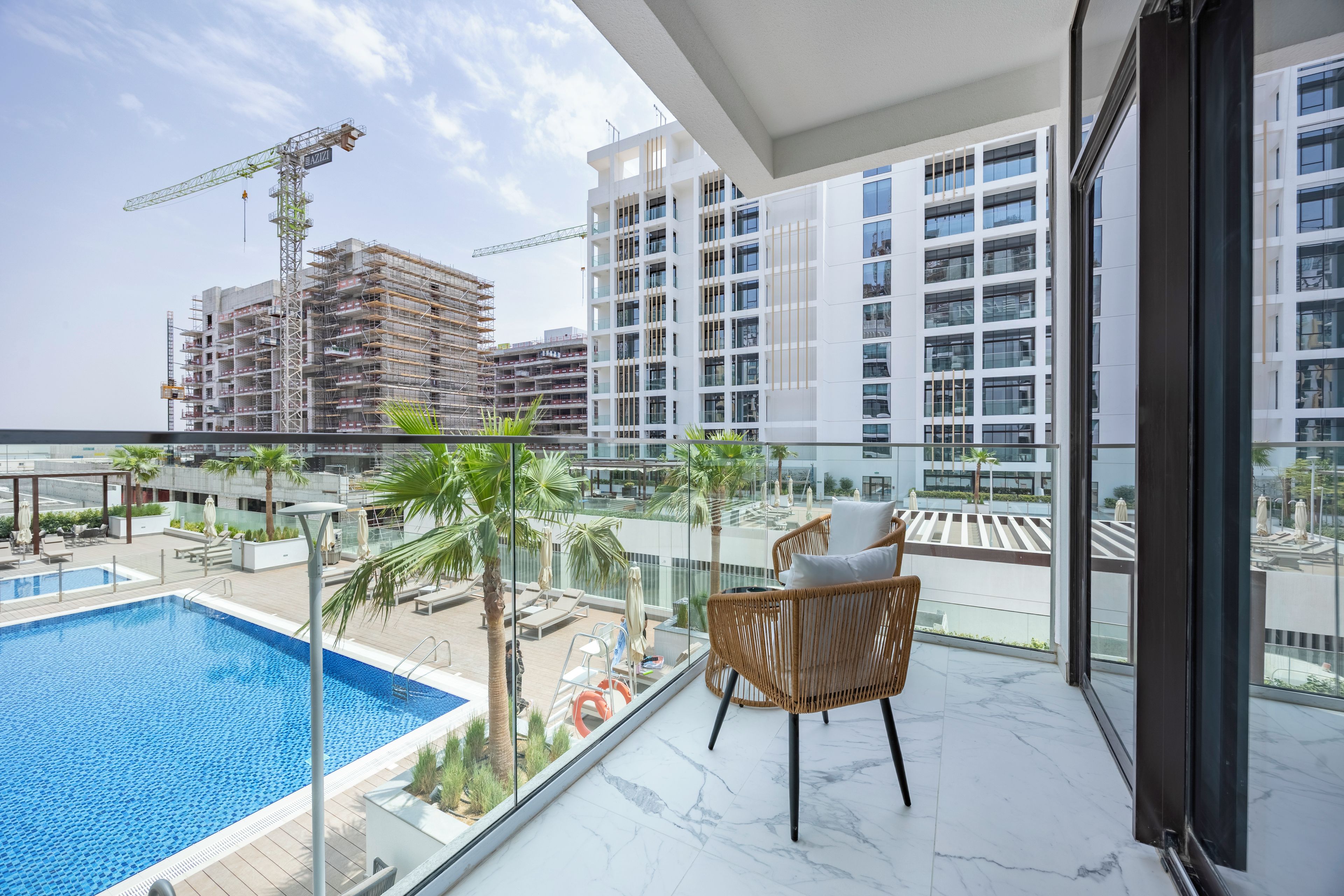A balcony with a view of a swimming pool, palm trees, and a construction site in the background.