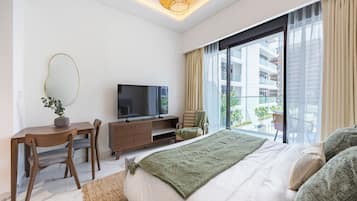 A modern hotel room with a large bed, a television, a desk with a chair, and a view of the outside balcony.