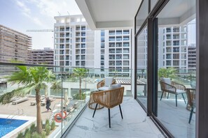 A balcony with a pool, lounge chairs, and a view of high-rise buildings. - Bloomfields Supreme Stu In Azizi (Dubai)