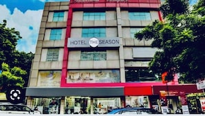 A hotel named 'Hotel The Season' with a red and beige facade, multiple windows, and a signboard. - Hotel The Season (Ahmedabad)