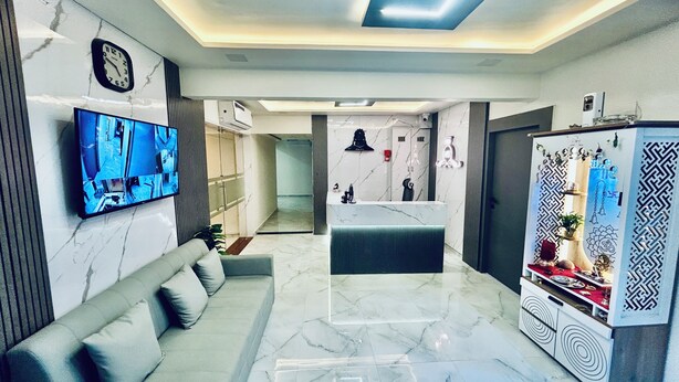 A modern living room with a flat-screen TV, a sofa, a kitchen area with a refrigerator, and a patterned wall. - Hotel The Season (Ahmedabad)