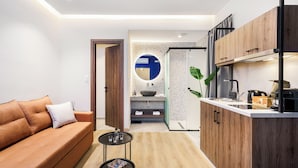 Un soggiorno moderno con un divano, un piccolo tavolino e un angolo cottura con pensili in legno e un lavello.