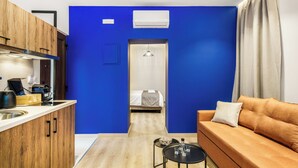 Camera d'albergo compatta con angolo cottura, un letto con testiera bianca, un divano marrone e un tavolino con bicchieri.