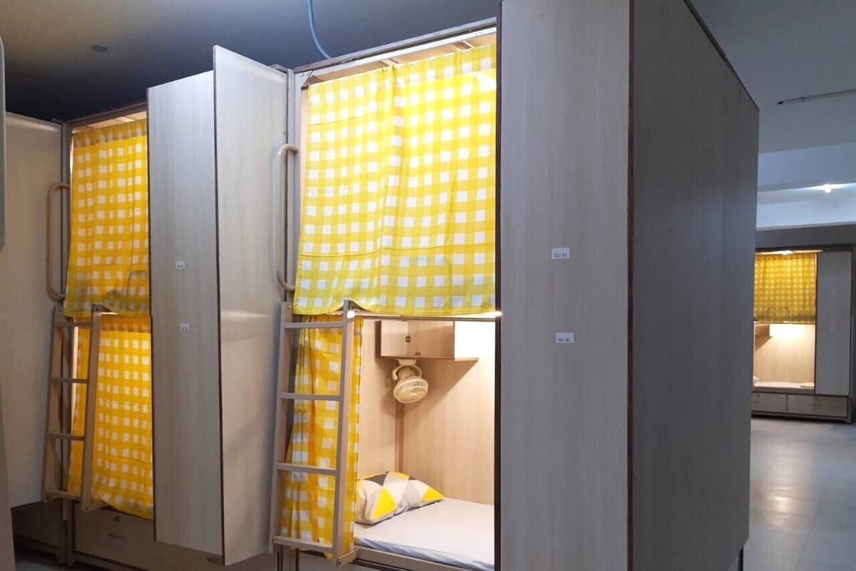 A row of bunk beds with yellow checkered curtains, each with a small shelf and a basket.