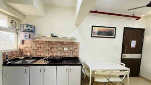 Een praktische keuken met een gasfornuis, witte kastjes, een kleine eettafel met stoelen, een raam en een deur.