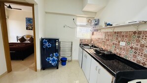 Een kleine keuken met een koelkast, een fornuis en een gootsteen. Een bed is zichtbaar in de aangrenzende kamer.