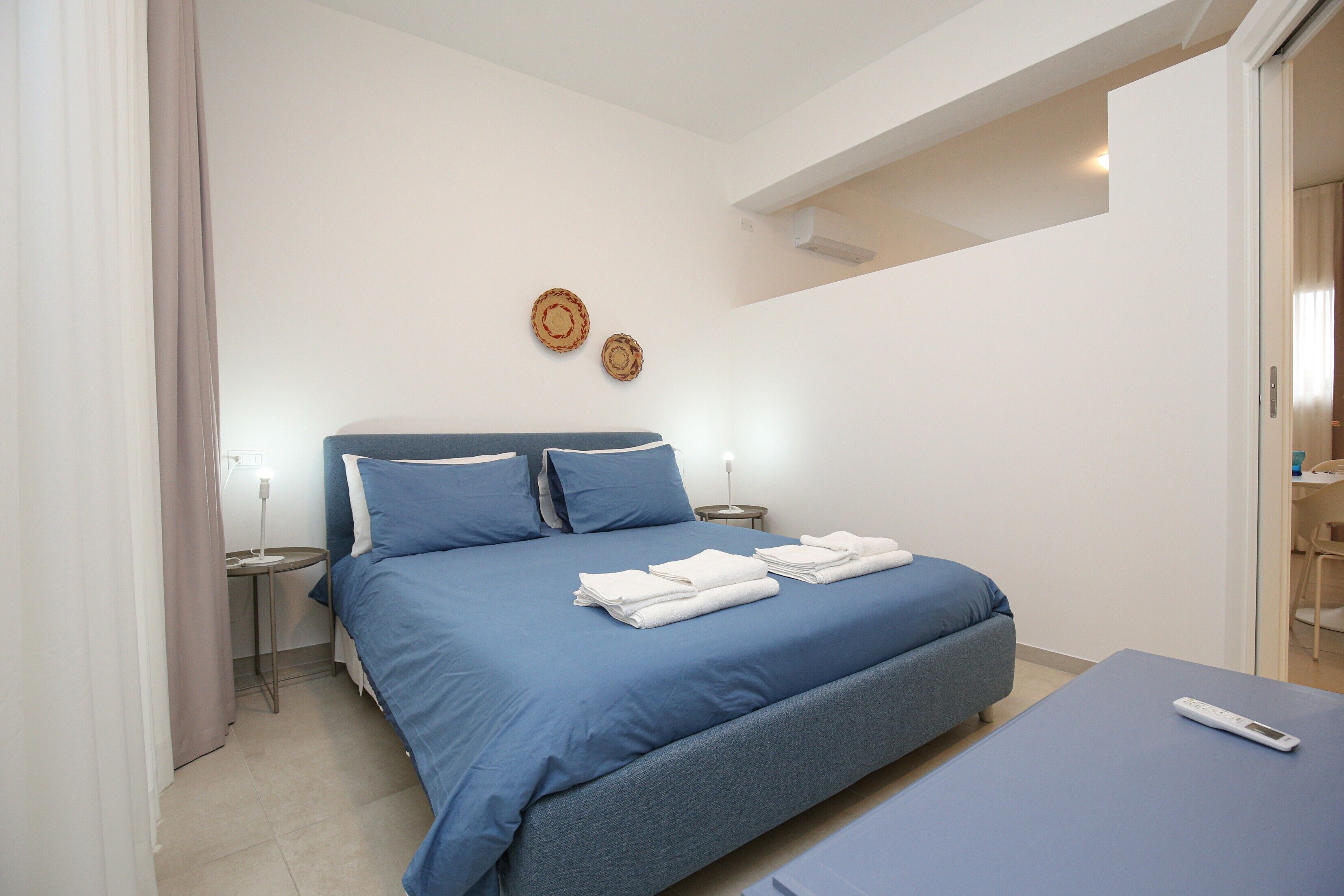 Un dormitorio con cama, mesitas de noche y una pequeña mesa con lámpara.
