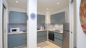 A compact kitchen with grey cabinets, a microwave, a kettle, a sink, and a refrigerator.