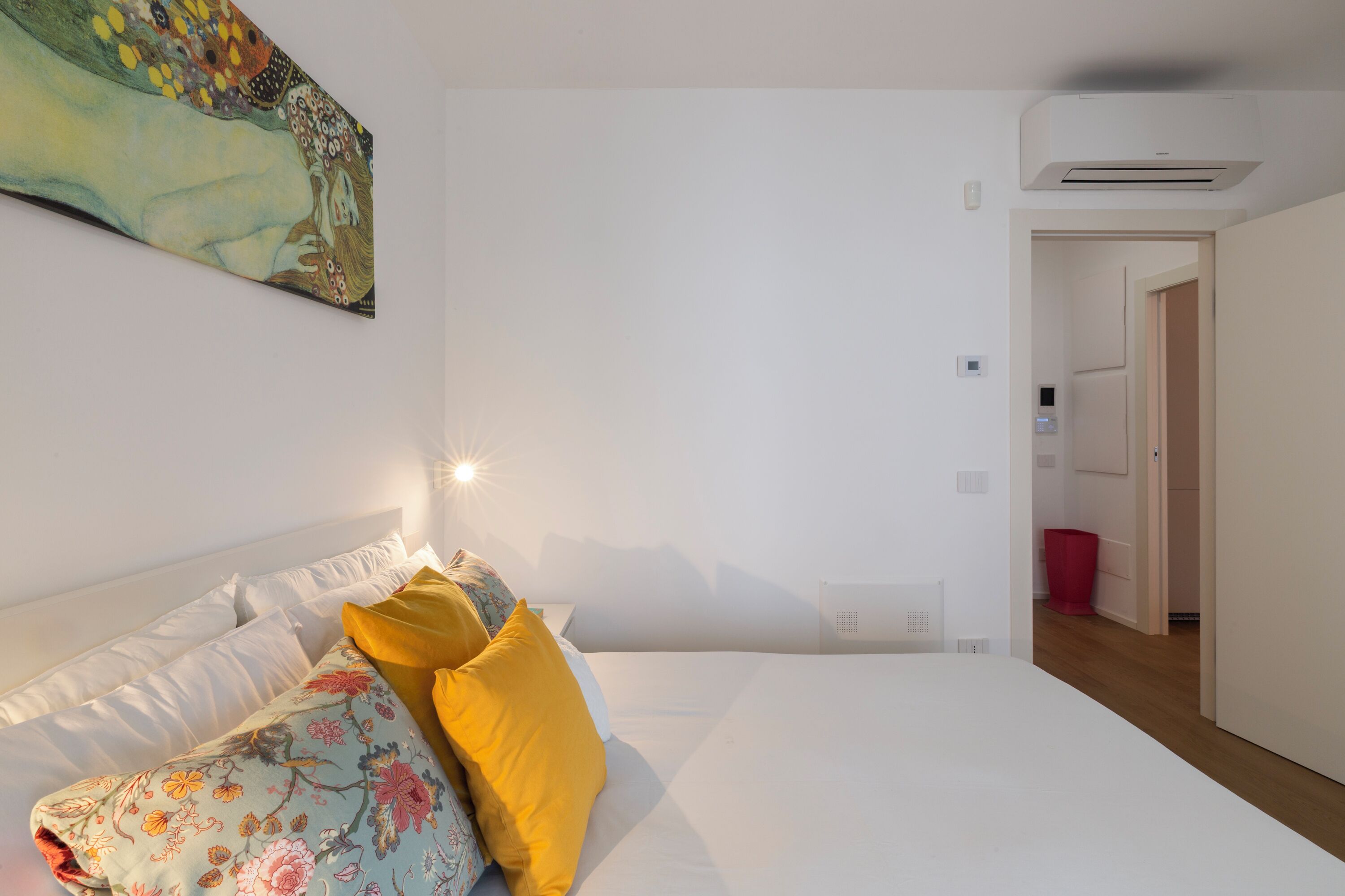 A bedroom with a bed, a nightstand, a wall-mounted air conditioner, and a door leading to another room.