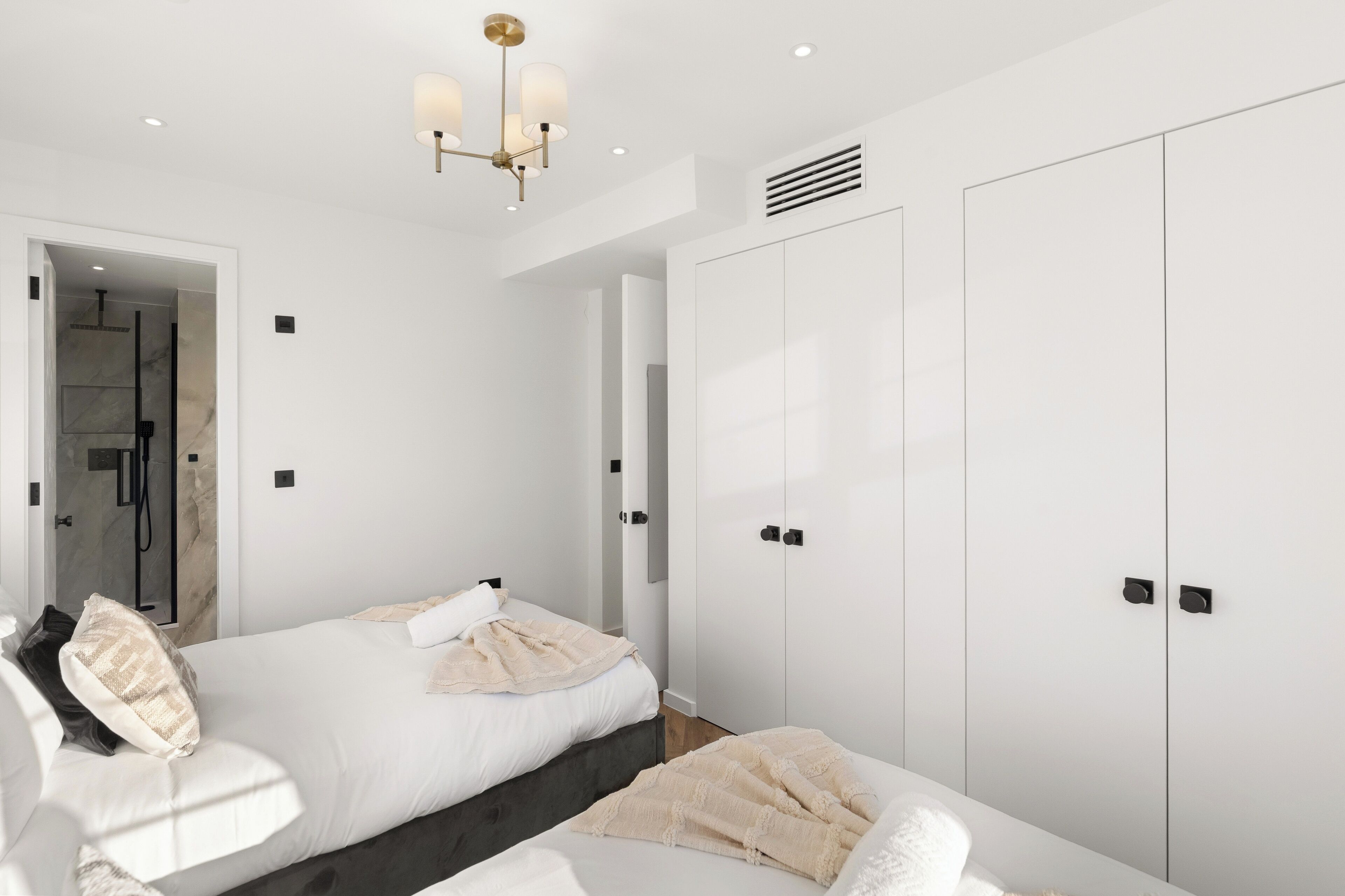 A modern bedroom with a bed, bedside tables, a wardrobe, and a shower area.