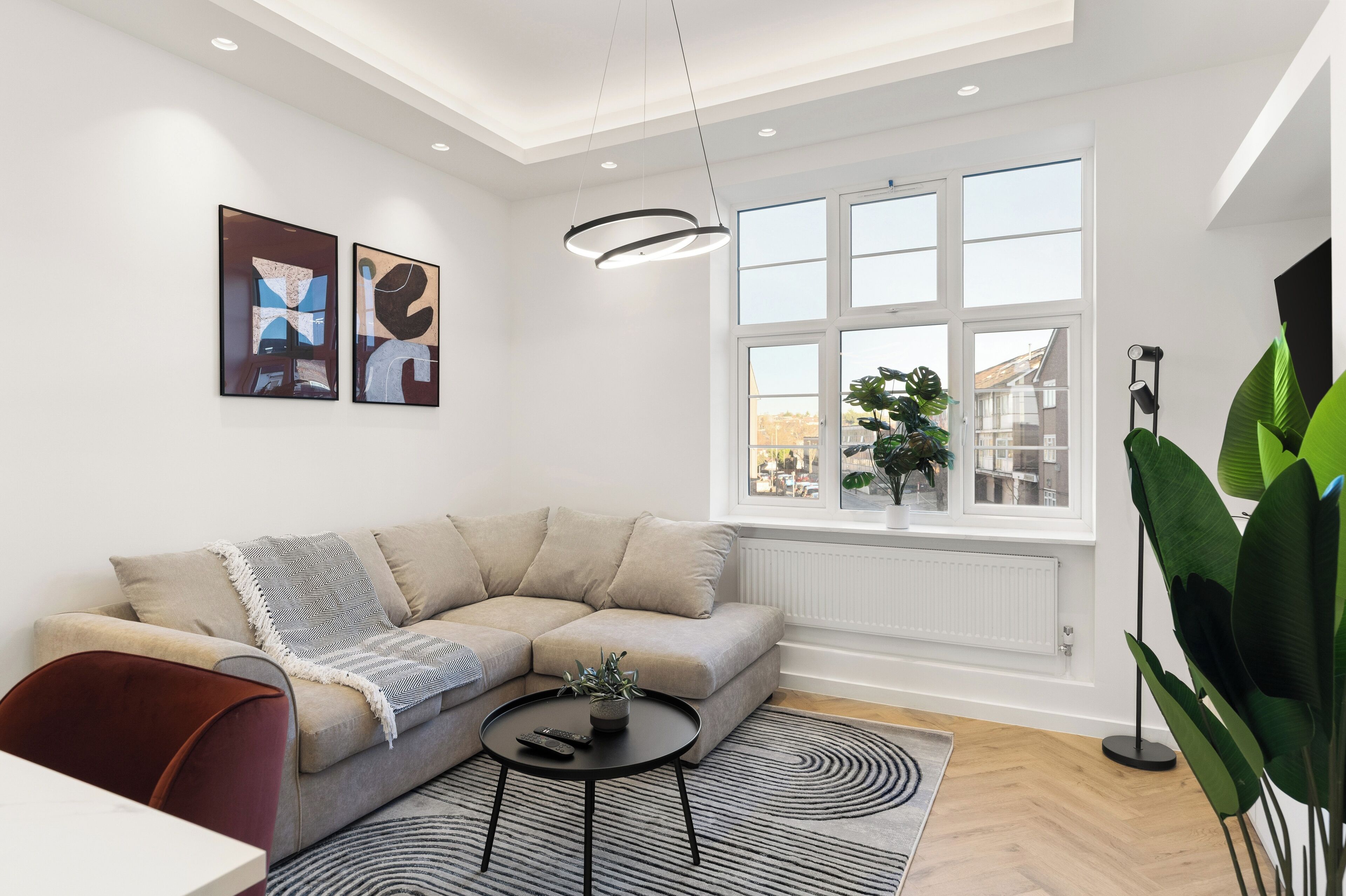 A modern living room with a sectional sofa, a round coffee table, and a large window with a view of buildings.