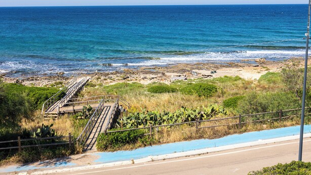 Eine Küstenstraße mit einer Holztreppe, die zu einem felsigen Strand führt.