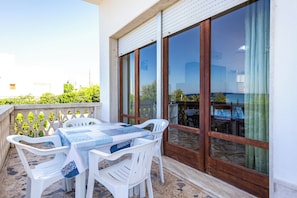 A balcony with a table and chairs, large windows, and a view of the sea. - Villetta Lelia (Torre Suda)