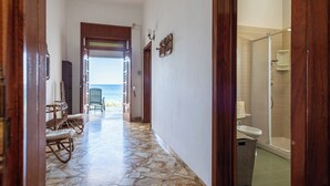 Ein Flur mit Fliesenboden, der zum Blick auf einen Strand führt, mit Holztüren und einem Duschbereich aus Glas.