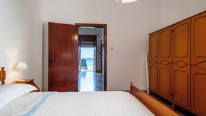 Ein Schlafzimmer mit einem großen Bett, einem Holzschrank und Blick durch eine offene Tür in einen Flur.