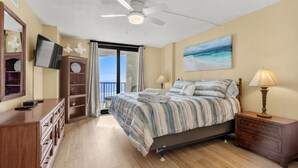 A bedroom with a bed, a ceiling fan, a TV, a dresser, a nightstand, and a painting. - 10% off weekly stays (Sat-Sat) thru Aug. 3BR 3BA OF condo. Crescent Beach. (North Myrtle Beach)