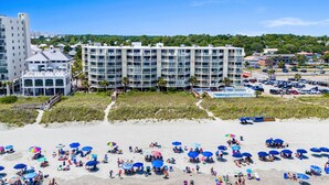 A beachfront hotel with multiple balconies, a pool area, and beach umbrellas. - 10% off weekly stays (Sat-Sat) thru Aug. 3BR 3BA OF condo. Crescent Beach. (North Myrtle Beach)