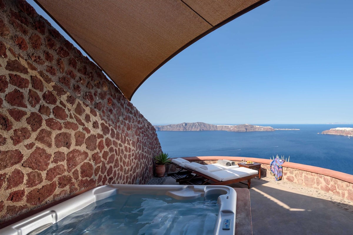 A stone wall with a hot tub and lounge chairs overlooking a scenic coastal view.