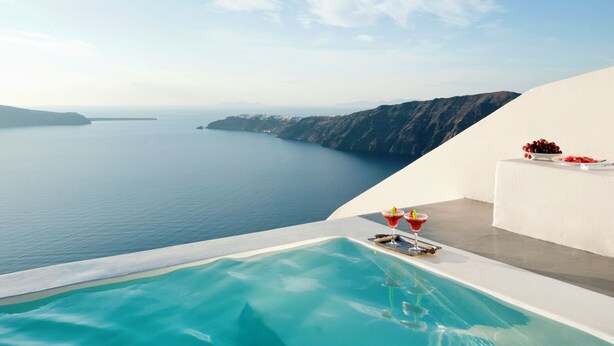 A clear blue sky, a large infinity pool, and a view of the sea and distant islands. - Anastasis Apartments and Spa (Santorini)