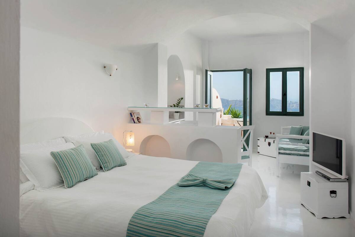 A modern bedroom with a large bed, a TV, and a balcony with a view.