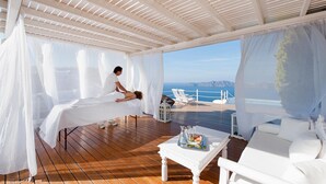 A spa area with a massage table, white furniture, and a view of the sea. - Anastasis Apartments and Spa (Santorini)