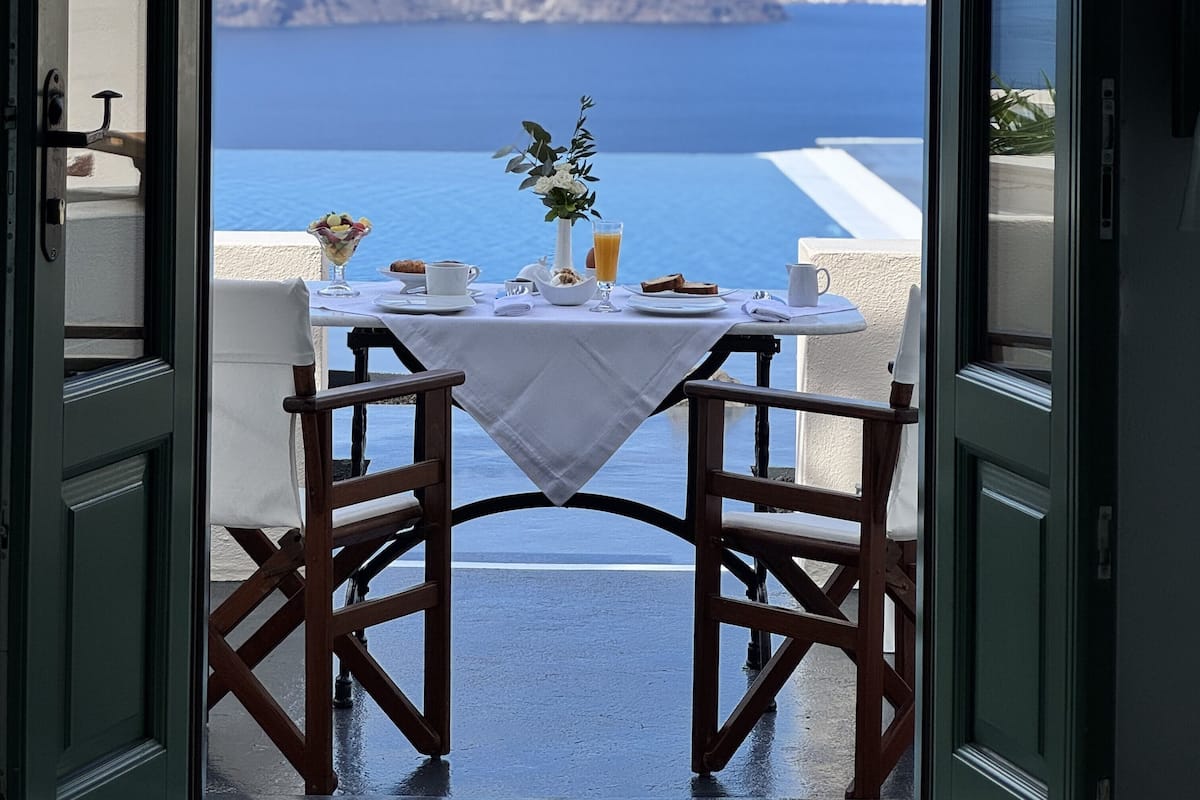 An open door leading to a table set with breakfast items and a view of the sea.