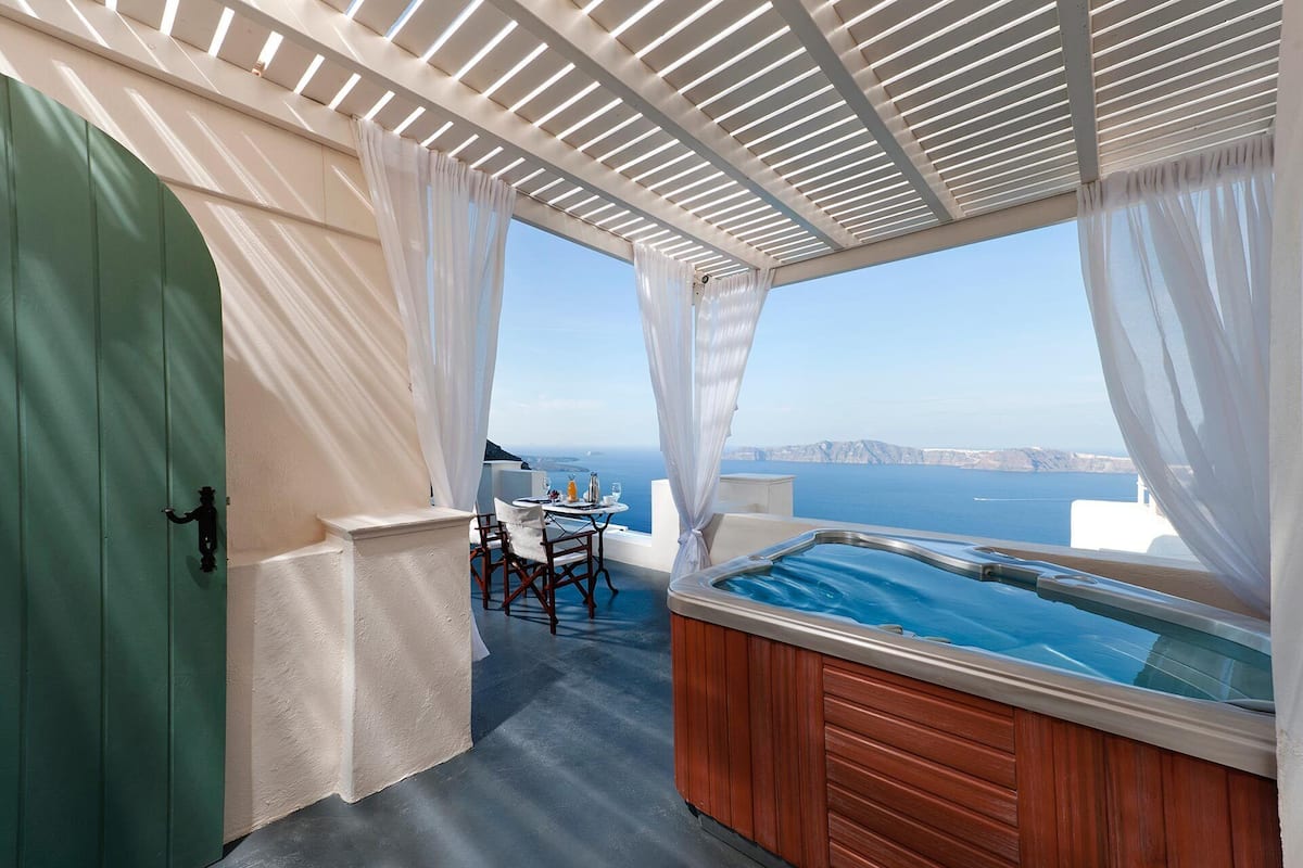 A balcony with a hot tub, a table with chairs, and a view of the sea.