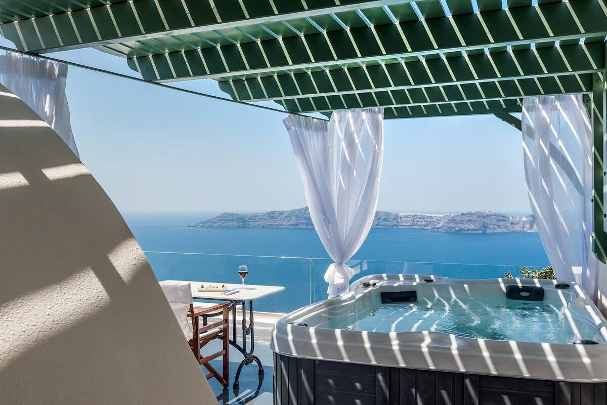 A hot tub with a view of the sea, a table with a glass of wine, and a chair.