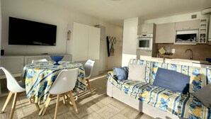 Een moderne keuken met een magnetron, oven en spoelbak. Er is een eethoek met een tafel en stoelen, en een bank met een bloemenprint.