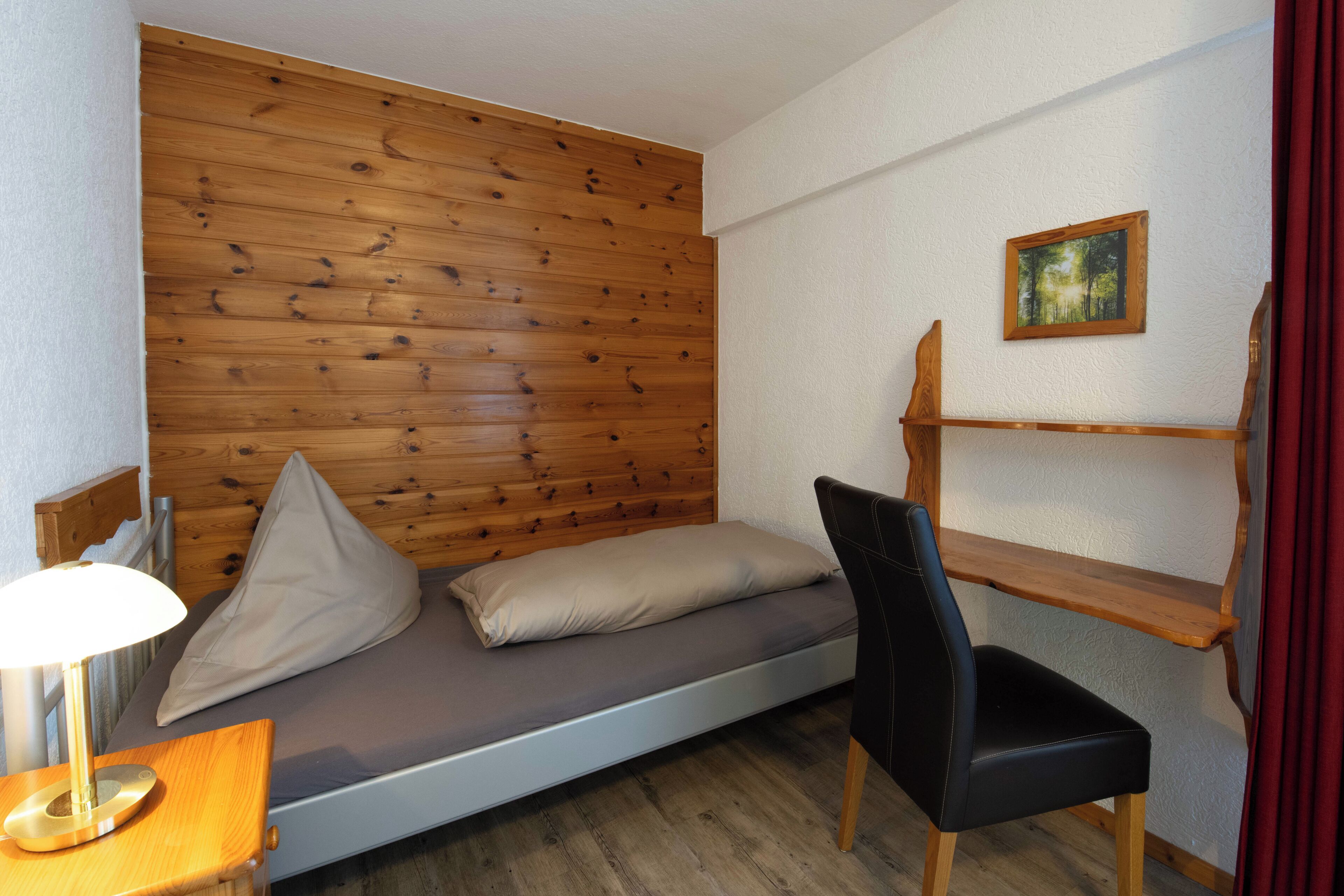 Una habitación pequeña con cama, una silla, un escritorio y una estantería.