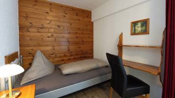 Una habitación pequeña con cama, una silla, un escritorio y una estantería.
